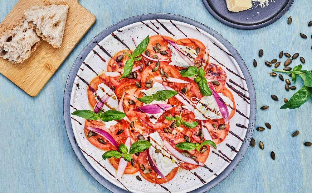 Tomatcarpaccio med kremet mozarella, gresskarkjerner og basilikum